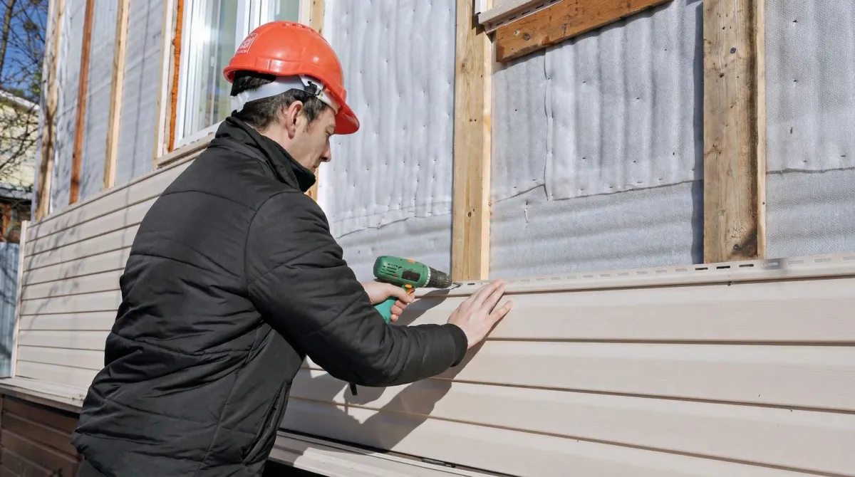 Siding replacement professional using a power drill to install new tan vinyl siding on a home exterior in Jacksonville, FL